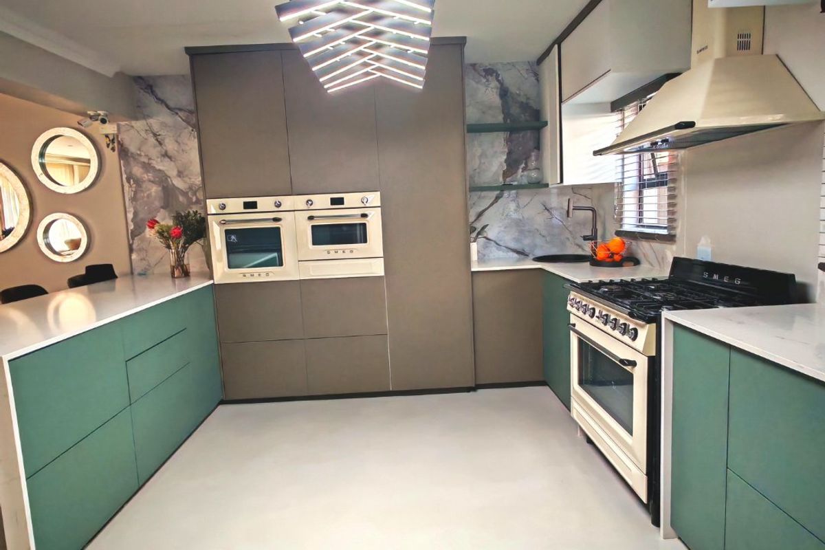 Modern kitchen featuring high-end Smeg appliances, custom green cabinetry, stone countertops, and a striking contemporary light fixture.