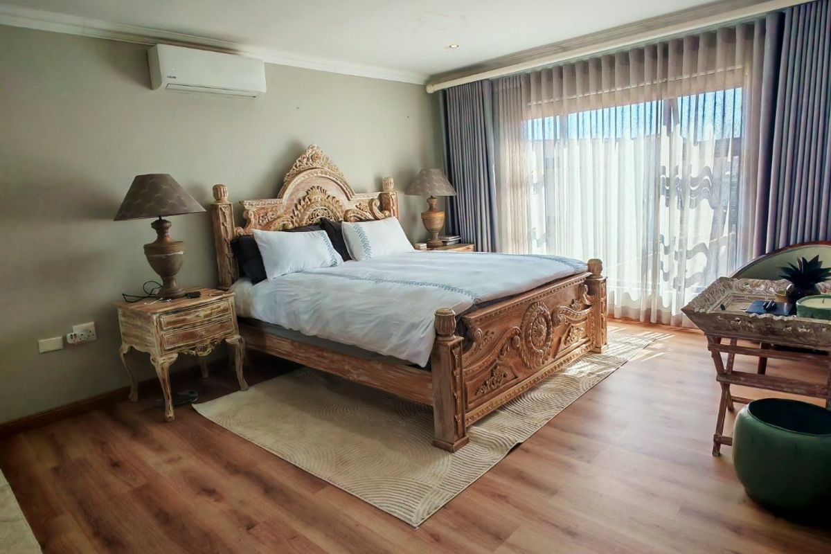 Spacious bedroom featuring laminate flooring, recessed lighting, a wall-mounted air conditioning unit, and large sliding glass doors with elegant sheer curtains.