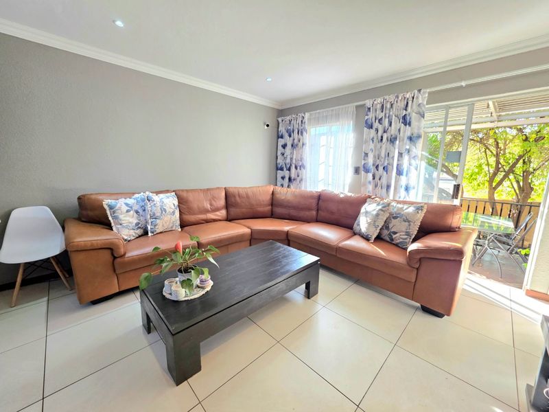 A bright living room featuring large format floor tiles, recessed downlighting, and a sliding glass door providing access to an outdoor patio area.