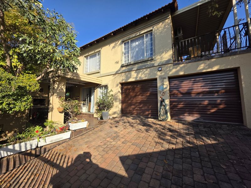 Front elevation of a double-story townhouse featuring a paved driveway, double roll-up garage doors, and an upper-level covered balcony.