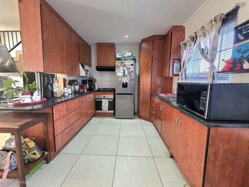 A functional kitchen featuring warm-toned wooden cabinetry, granite countertops, tiled flooring, and integrated appliances including a gas hob and oven.