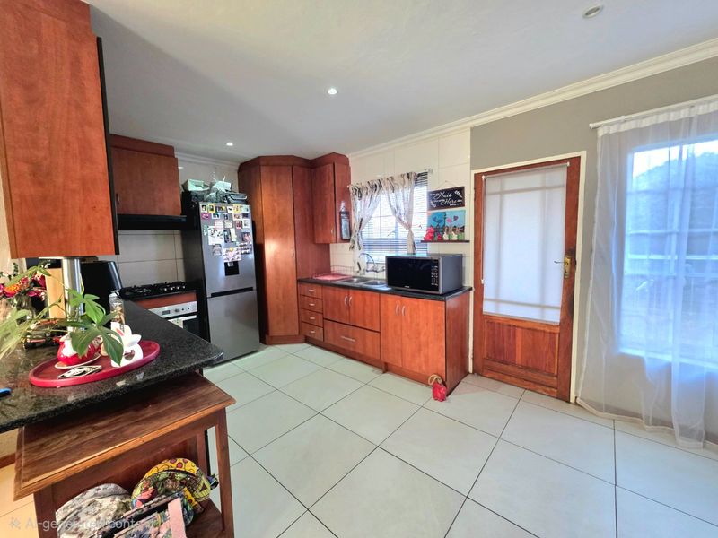 Functional kitchen featuring warm-toned wooden cabinetry, granite countertops, tiled flooring, and direct access to the exterior via a timber door.