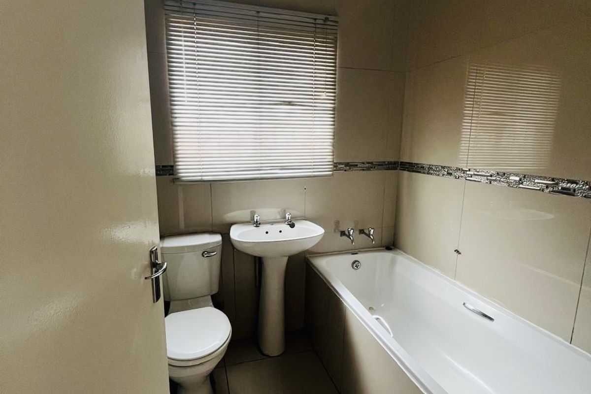 A functional bathroom featuring a pedestal basin, toilet, and bathtub with neutral wall and floor tiling.
