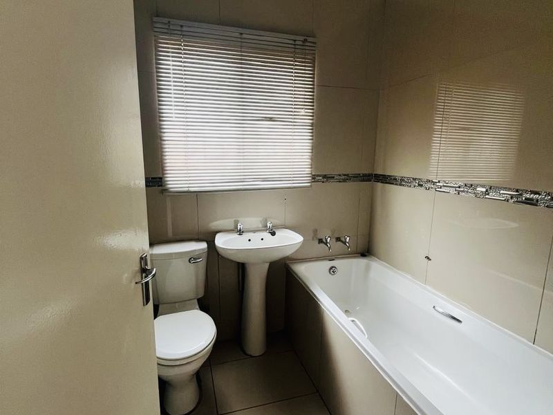 A functional bathroom featuring a pedestal basin, toilet, and bathtub with neutral wall and floor tiling.