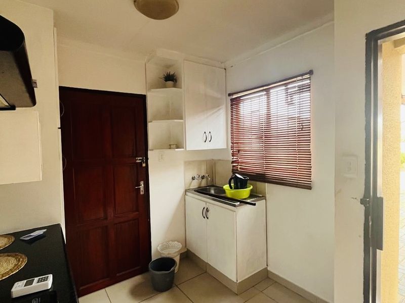 A functional scullery area featuring built-in cabinetry, a stainless steel sink, tiled flooring, and direct access to the exterior.