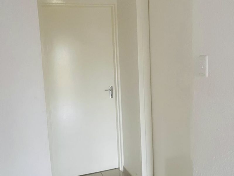 A simple, neutral hallway featuring tiled flooring and two internal doors, providing access to adjacent rooms.