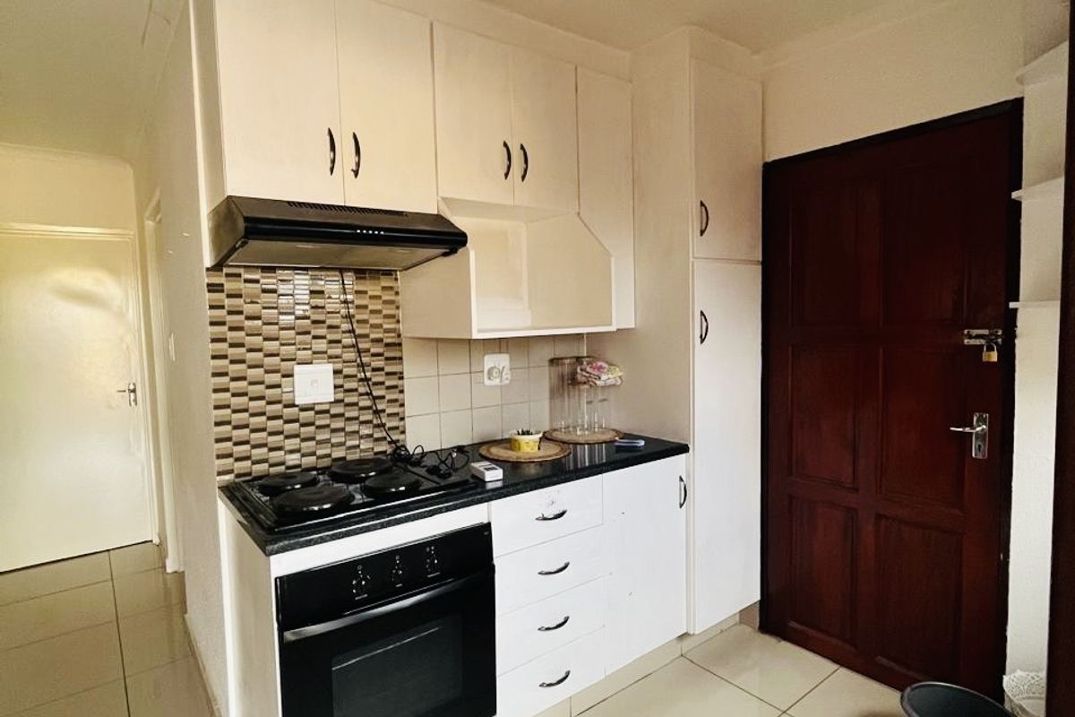 Compact kitchen featuring white built-in cabinetry, a built-in oven with hob, extractor fan, tiled splashback, and neutral floor tiles.