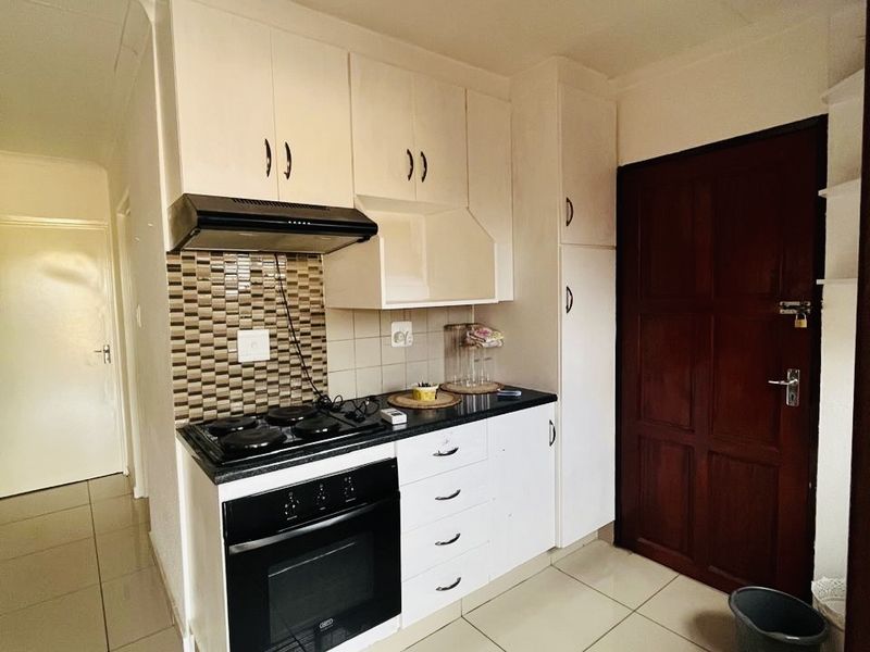 Compact kitchen featuring white built-in cabinetry, a built-in oven with hob, extractor fan, tiled splashback, and neutral floor tiles.