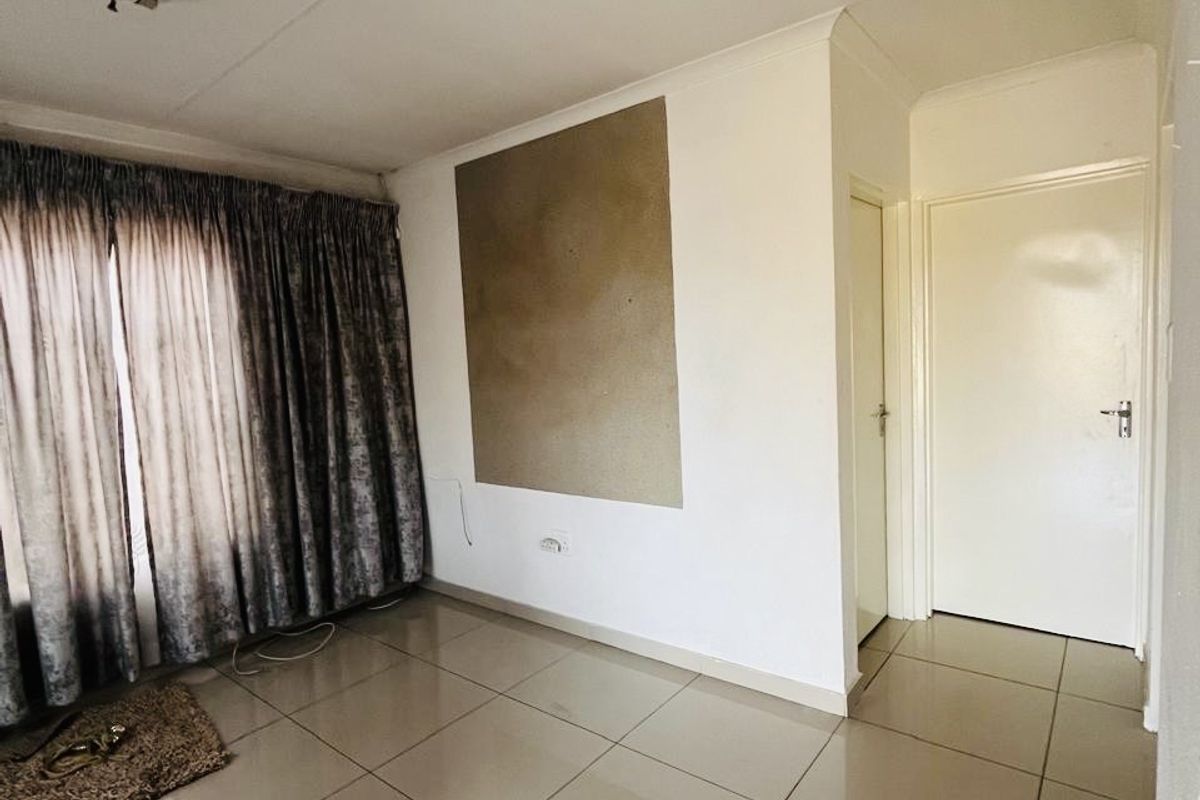 An empty living room featuring neutral tiled flooring, coved ceilings, and internal doors, presenting a blank canvas for potential interior updates.