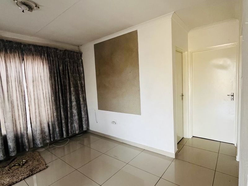 An empty living room featuring neutral tiled flooring, coved ceilings, and internal doors, presenting a blank canvas for potential interior updates.