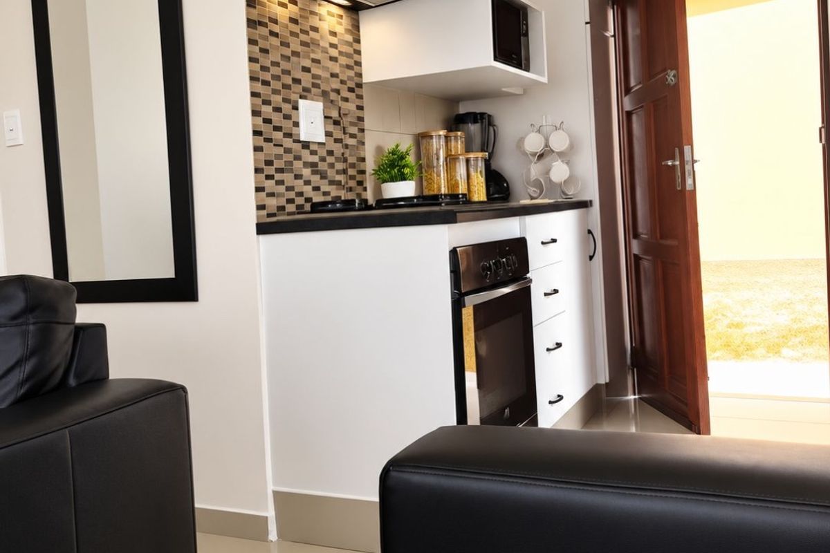 Compact kitchen area featuring modern white cabinetry, built-in oven, extractor fan, and a decorative tiled backsplash, seamlessly integrated into the living space.