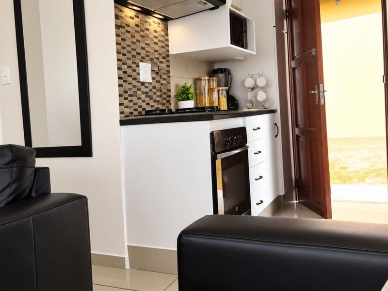 Compact kitchen area featuring modern white cabinetry, built-in oven, extractor fan, and a decorative tiled backsplash, seamlessly integrated into the living space.