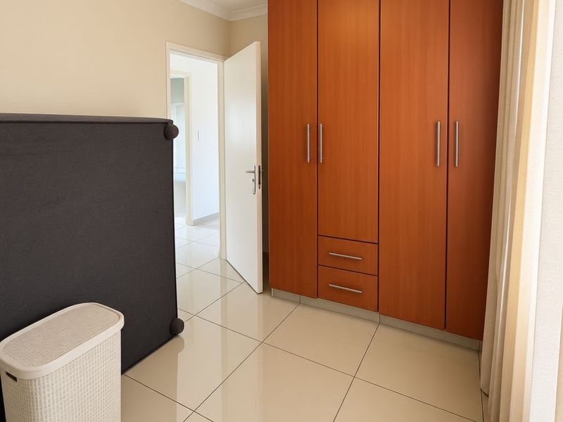A bedroom featuring large format floor tiles and a substantial built-in wooden wardrobe with integrated drawers.