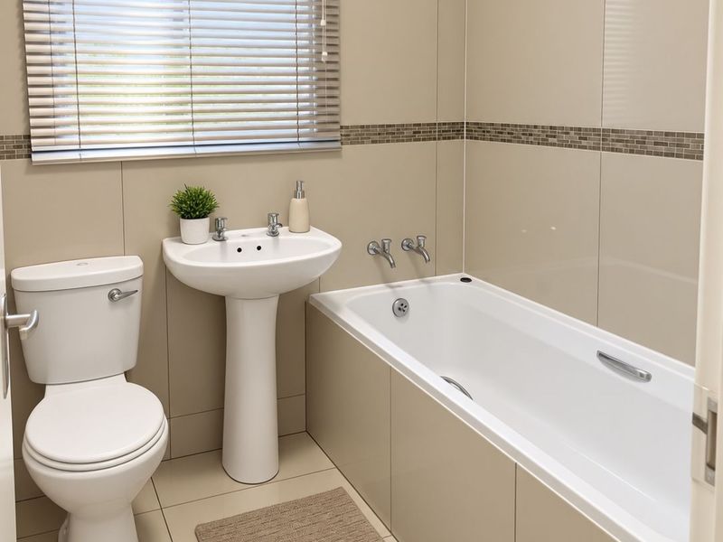 A clean, modern bathroom featuring neutral wall and floor tiles, a pedestal basin, a standard toilet, and a built-in bathtub.