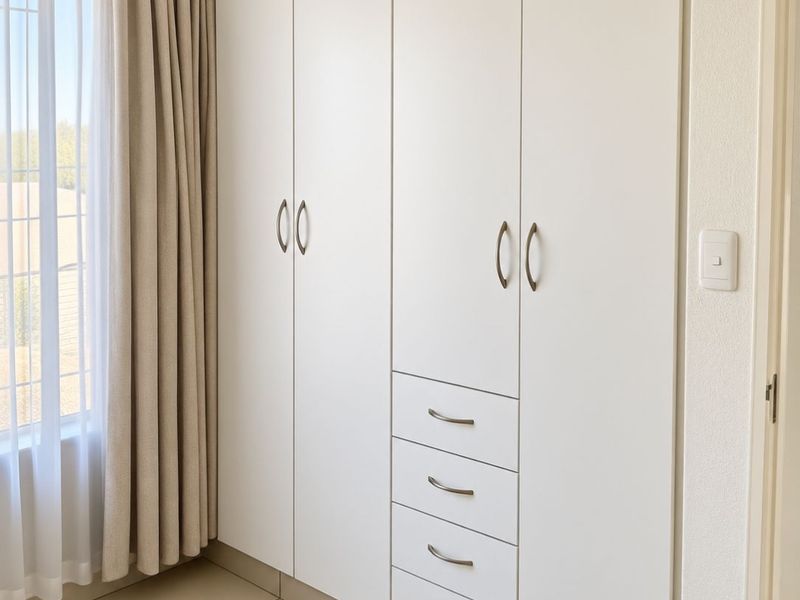 A clean, modern bedroom featuring neutral tiled flooring and ample built-in white cabinetry with integrated drawers.