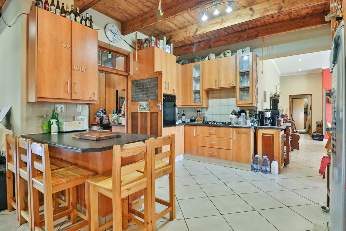 A rustic kitchen featuring wooden cabinetry, exposed timber ceiling beams, a built-in oven, gas hob, and a functional breakfast counter with tiled flooring.