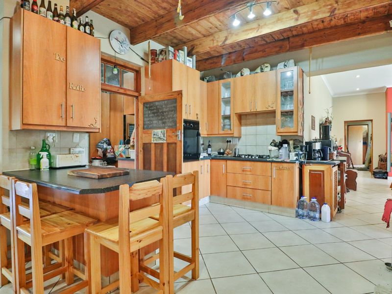 A rustic kitchen featuring wooden cabinetry, exposed timber ceiling beams, a built-in oven, gas hob, and a functional breakfast counter with tiled flooring.