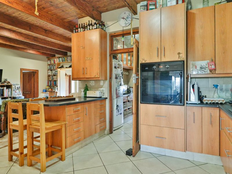 A rustic kitchen featuring wooden cabinetry, exposed timber ceiling beams, tiled floors, and a built-in oven, with an adjacent open-plan living area.