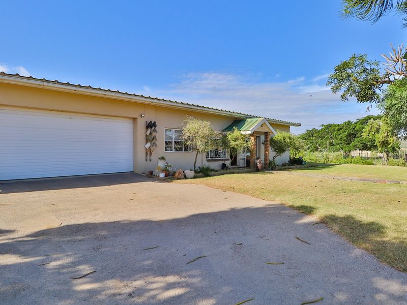 Front exterior view of a farm property featuring a single garage, concrete driveway, and established garden area under a metal roof structure.