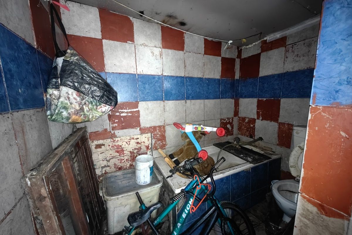 A bathroom in poor condition requiring significant renovation, featuring a bathtub, toilet, and dated, damaged wall tiling.