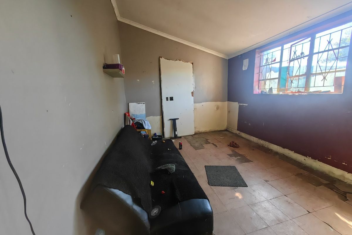 A living room space requiring significant renovation, featuring tiled flooring, security bars on windows, and walls in need of repair and repainting.