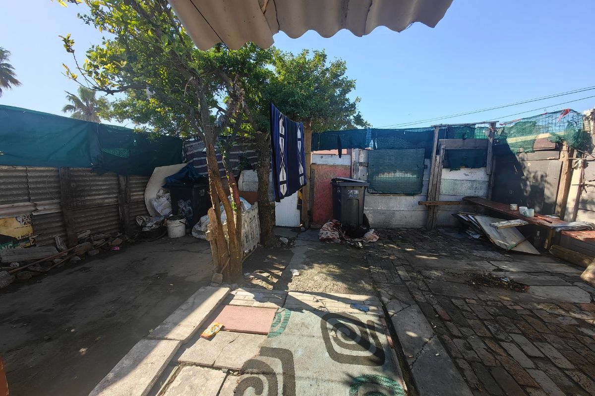 A rear outdoor area featuring paved surfaces, corrugated iron boundary fencing, and shade cloth screening, requiring significant maintenance and clearing.