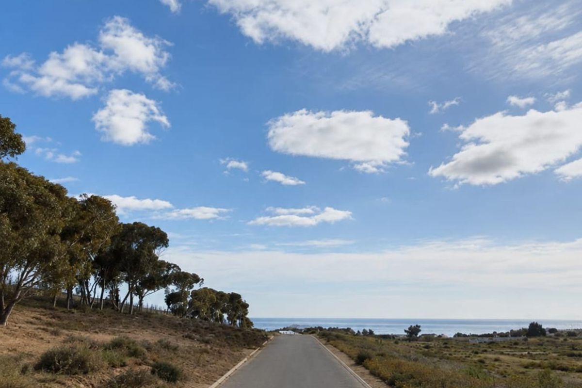 A paved access road leading towards the coastline, featuring natural landscape surroundings and clear ocean views.