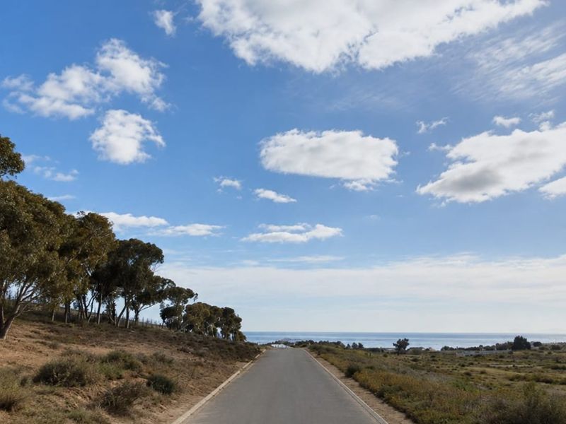 A paved access road leading towards the coastline, featuring natural landscape surroundings and clear ocean views.
