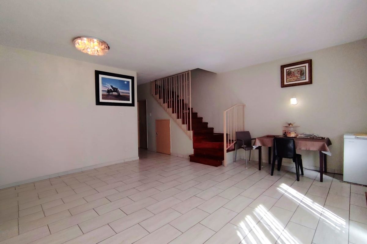 Open plan living area featuring light-colored floor tiles and a prominent wooden staircase with a metal balustrade.