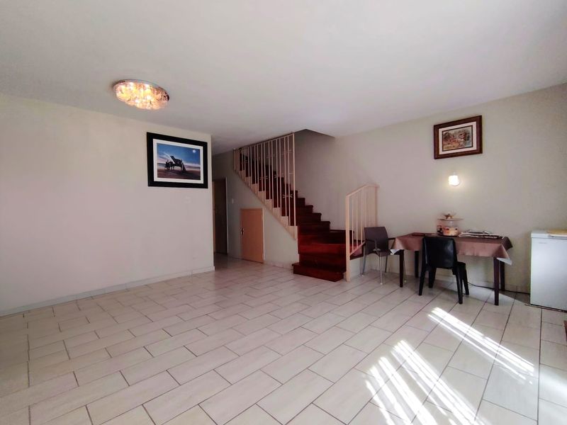 Open plan living area featuring light-colored floor tiles and a prominent wooden staircase with a metal balustrade.