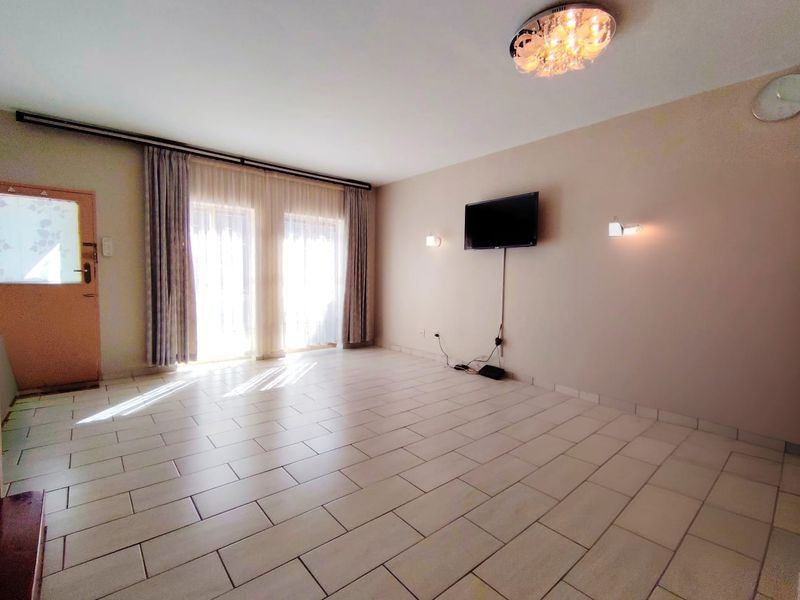 A spacious, empty living room featuring tiled flooring, wall-mounted lighting, and sliding glass doors that provide ample natural light.