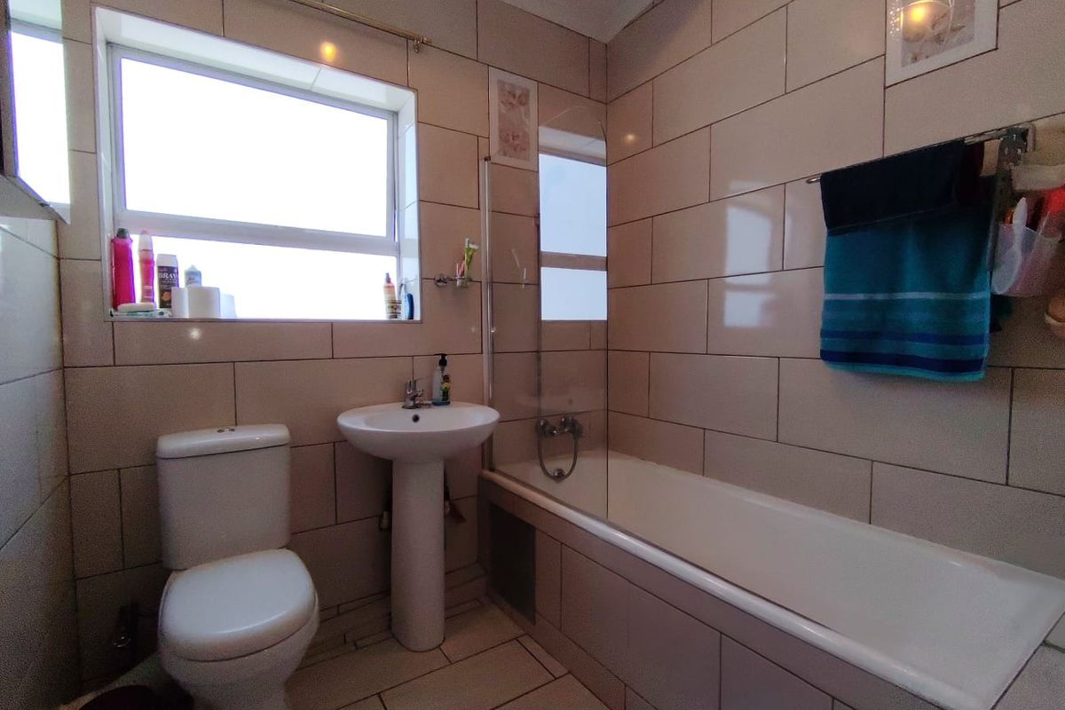 A functional bathroom featuring a pedestal basin, toilet, and a bathtub with a glass shower screen, finished with neutral wall and floor tiling.
