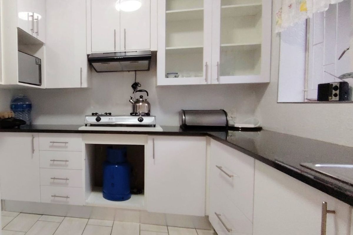 Modern kitchen featuring white gloss cabinetry, black granite countertops, gas hob, extractor fan, and built-in microwave with tiled flooring.