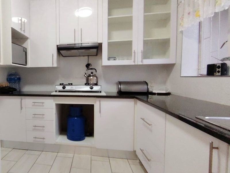 Modern kitchen featuring white gloss cabinetry, black granite countertops, gas hob, extractor fan, and built-in microwave with tiled flooring.