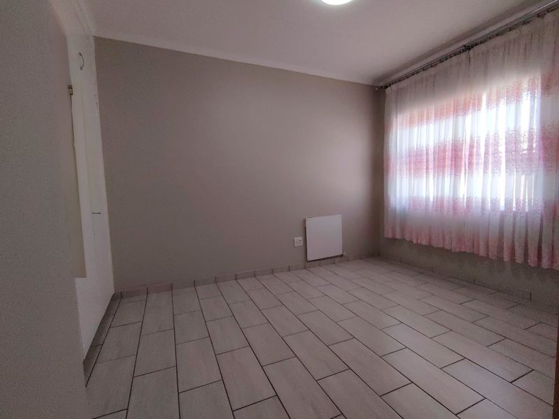 A clean, empty bedroom featuring neutral wall tones, tiled flooring, and a wall-mounted electric heater, ready for personalization.