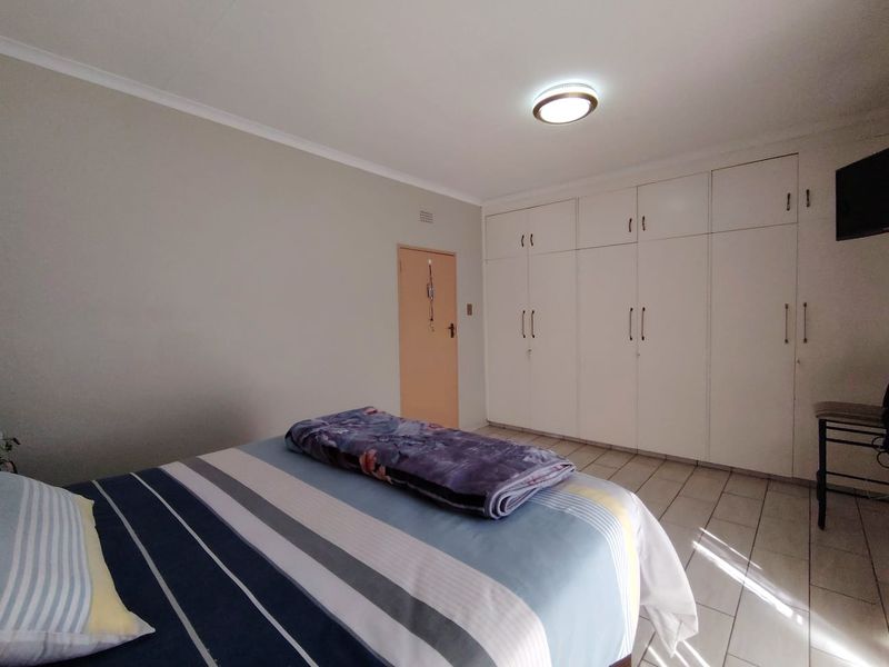 A bedroom featuring tiled flooring, built-in white cupboards, and a central ceiling light fixture.