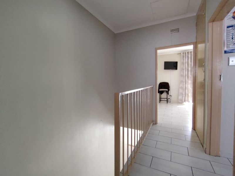 A functional hallway featuring tiled flooring and a metal balustrade, providing access to adjacent living spaces.