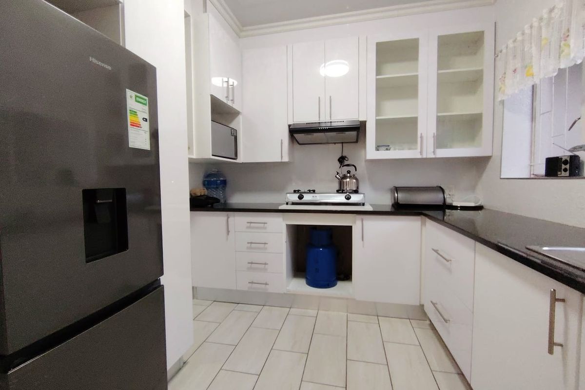 Modern kitchen featuring white cabinetry, black granite countertops, a gas hob, extractor fan, and built-in microwave with tiled flooring.