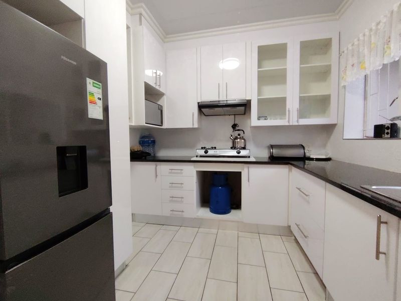 Modern kitchen featuring white cabinetry, black granite countertops, a gas hob, extractor fan, and built-in microwave with tiled flooring.