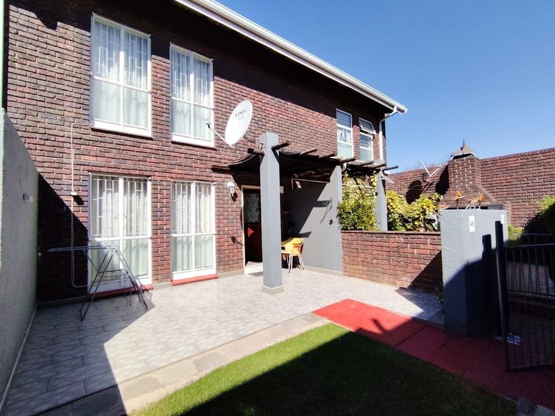 Rear exterior view of the apartment featuring a paved patio area, brick facade, and a pergola structure.