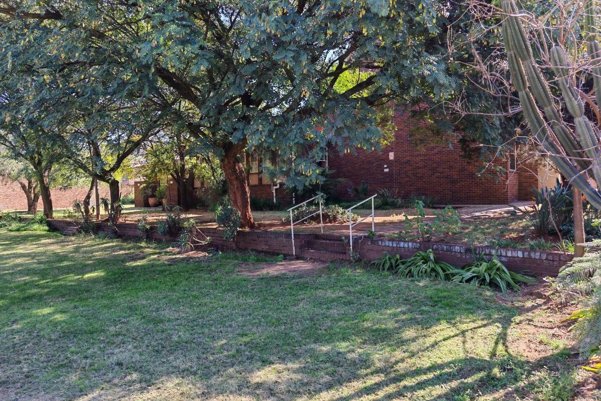 Rear exterior view of the commercial property featuring a brick facade, a paved patio area, and a tiered garden with a retaining wall.