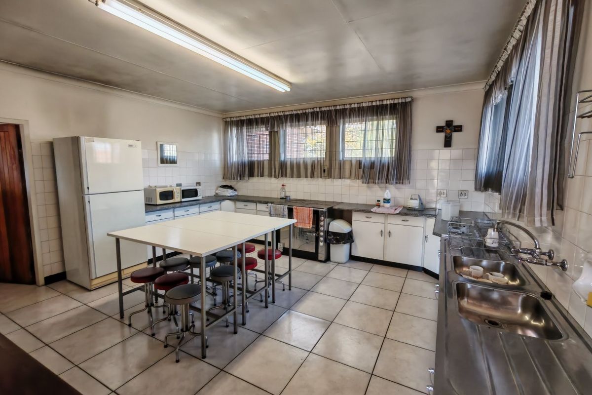 A functional commercial kitchen featuring tiled flooring, ample built-in cabinetry, a double stainless steel sink, and a freestanding stove with a tiled splashback.