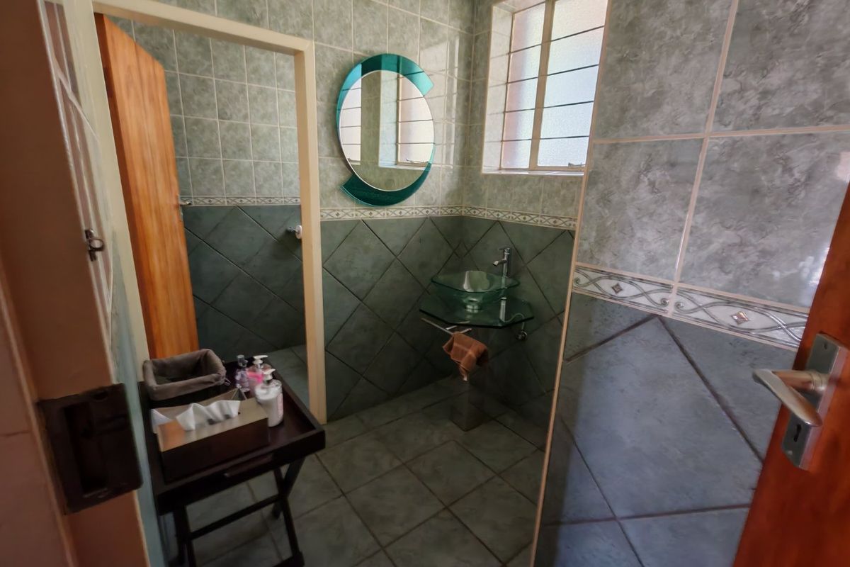 A compact bathroom featuring green tiled walls, a glass vessel sink with a wall-mounted faucet, and a window with security bars.