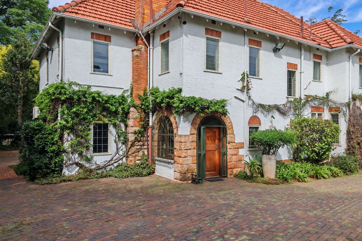A charming commercial property featuring a white brick facade, terracotta roof tiles, and a distinctive stone arched entrance with a paved brick driveway.