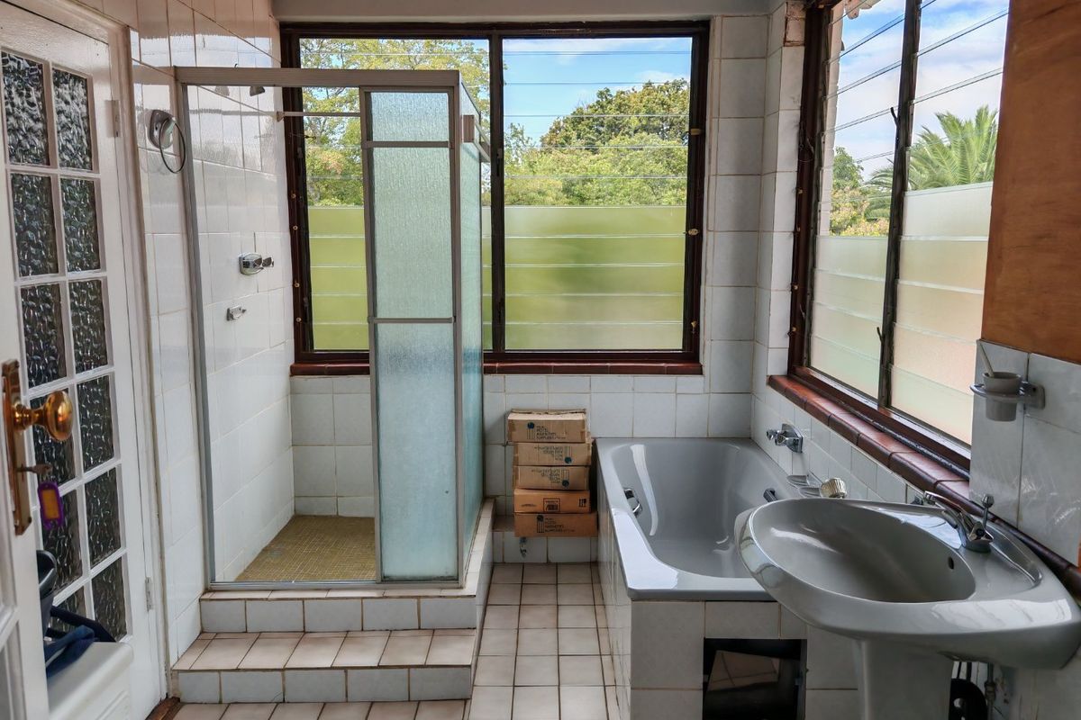 A dated bathroom featuring a built-in bathtub, separate shower enclosure, and pedestal basin, with large windows providing natural light.