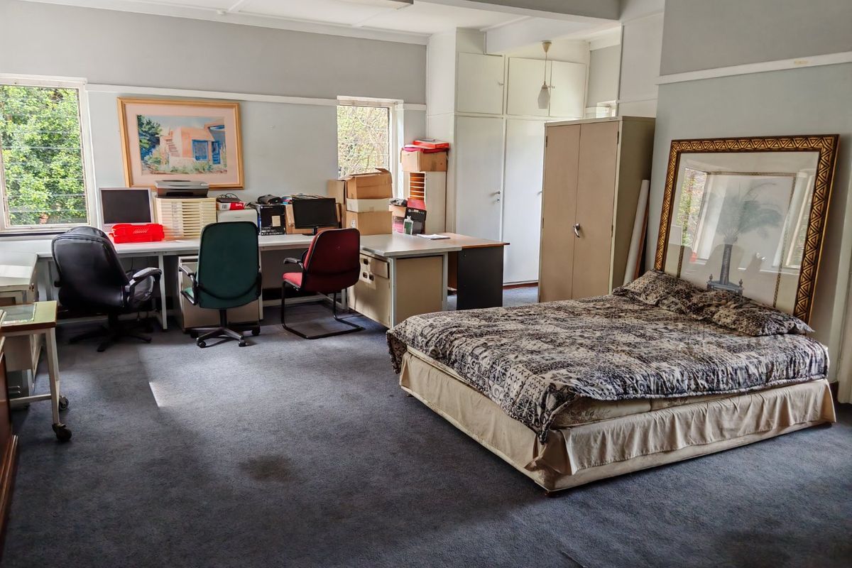 Spacious bedroom featuring built-in cupboards, carpet flooring, and a picture rail, currently utilized as a multi-purpose office and sleeping area.