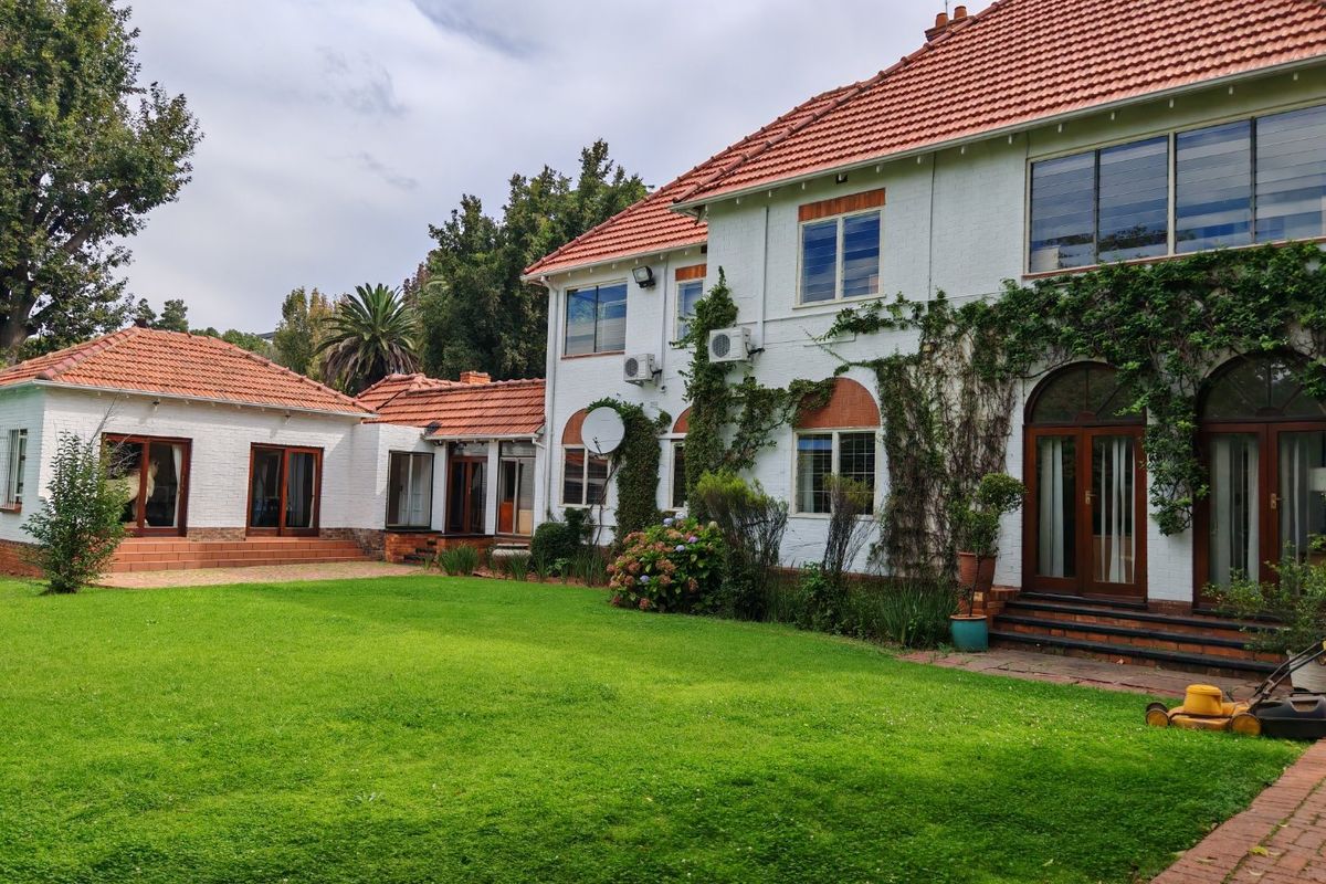 Rear view of a multi-story commercial property featuring a large lawn, paved patio areas, and traditional brick architecture with terracotta roof tiles.