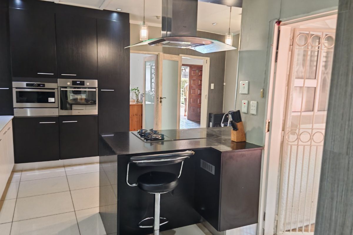 Modern kitchen featuring dark cabinetry, built-in oven and microwave, a central island with a gas hob, and sleek tiled flooring.