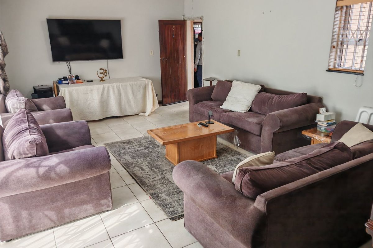 A living room featuring tiled flooring, a timber door, and a window with security grilles, offering a functional space with potential for cosmetic updates.
