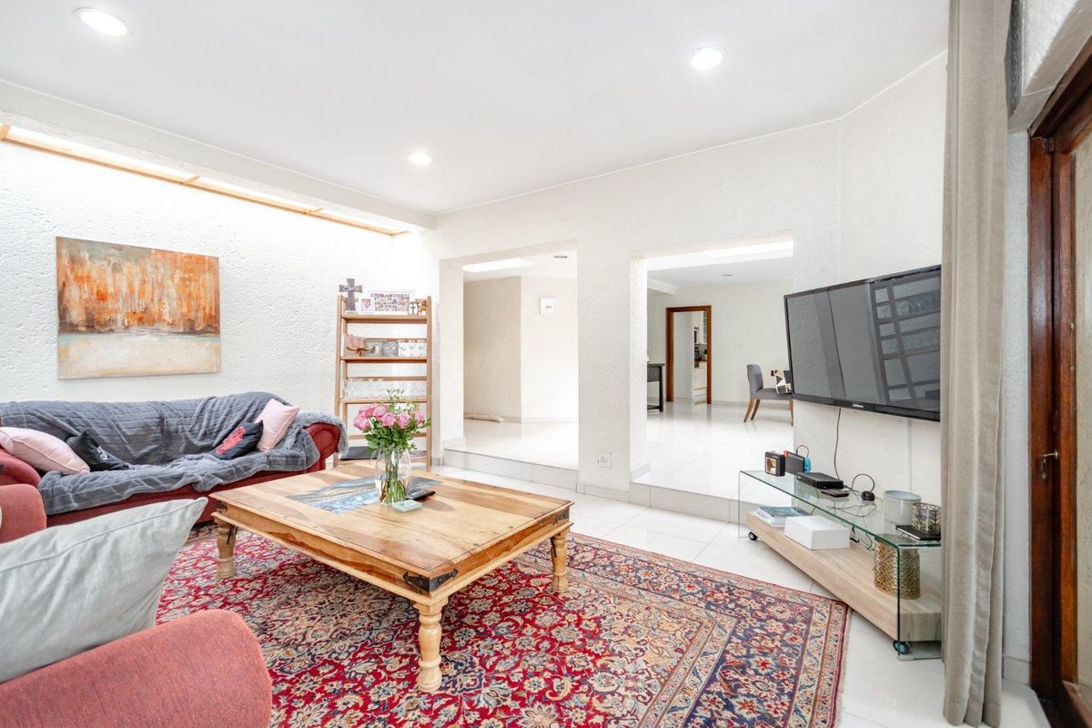 Spacious living room featuring bright tiled flooring, recessed downlighting, and a textured wall finish, with an open-plan layout leading to adjacent living areas.